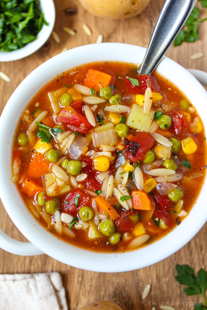 Vegan vegetable orzo soup in a small white bowl with fresh parsley