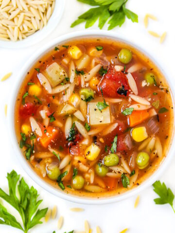 Vegan vegetable orzo soup in a small white bowl with fresh parsley