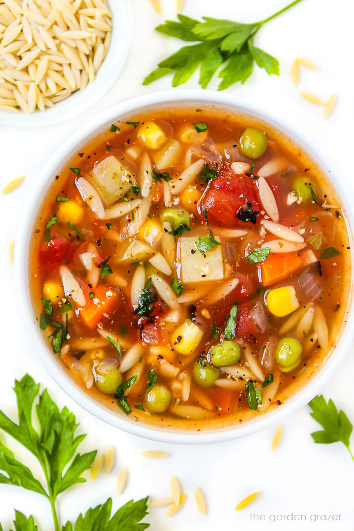 Vegan vegetable orzo soup in a small white bowl with fresh parsley