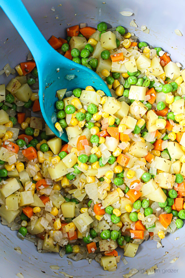 Overhead view of onion, potato, carrots, peas, and garlic cooking in a large pot with spoon