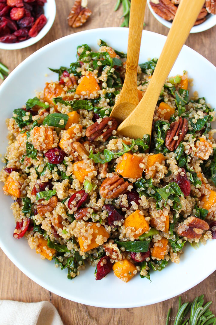 Fall harvest quinoa salad in a white serving bowl with wooden spoons