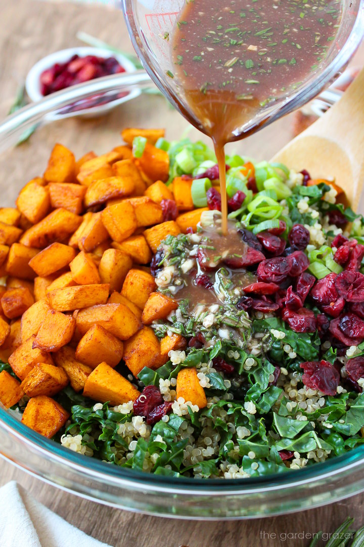 Rosemary maple balsamic dressing being poured over fall quinoa salad ingredients prepared in a glass mixing bowl