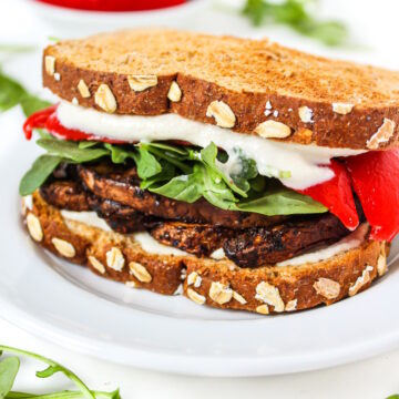Vegan portabella mushroom sandwich with red pepper and arugula on a white plate