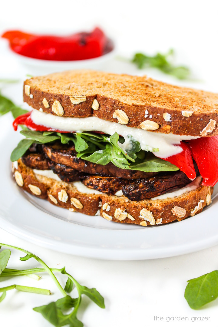 Vegan portabella mushroom sandwich with red pepper and arugula on a white plate