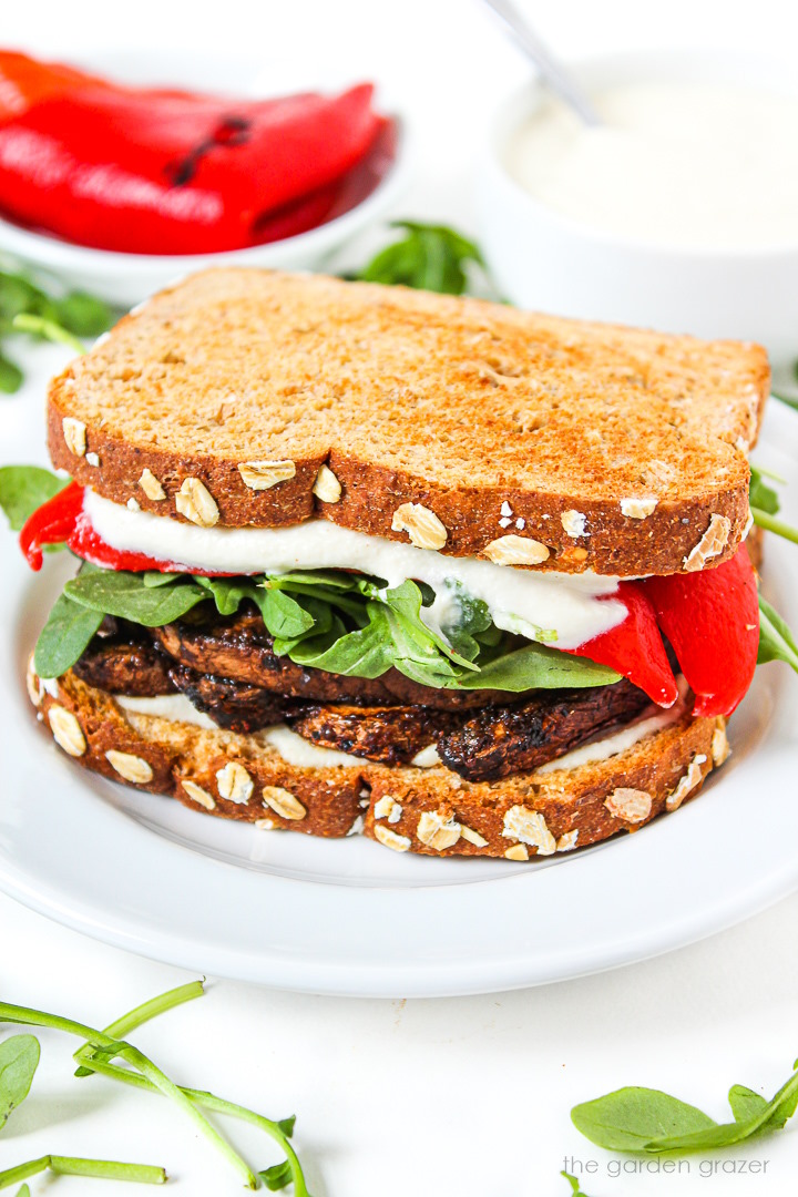 Portabella mushroom sandwich on a white plate with roasted red pepper, arugula, and garlic aioli sauce