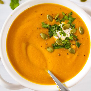 A small spoon lifting up vegan pumpkin curry soup in a white serving bowl