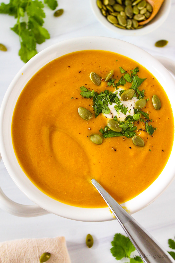 A small spoon lifting up vegan pumpkin curry soup in a white serving bowl