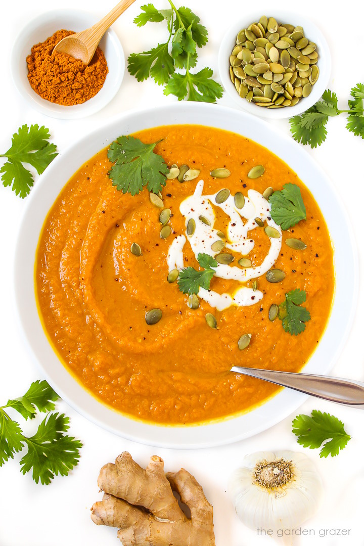 Overhead view of vegan pumpkin curry soup in a white bowl topped with yogurt, pumpkin seeds, and fresh cilantro