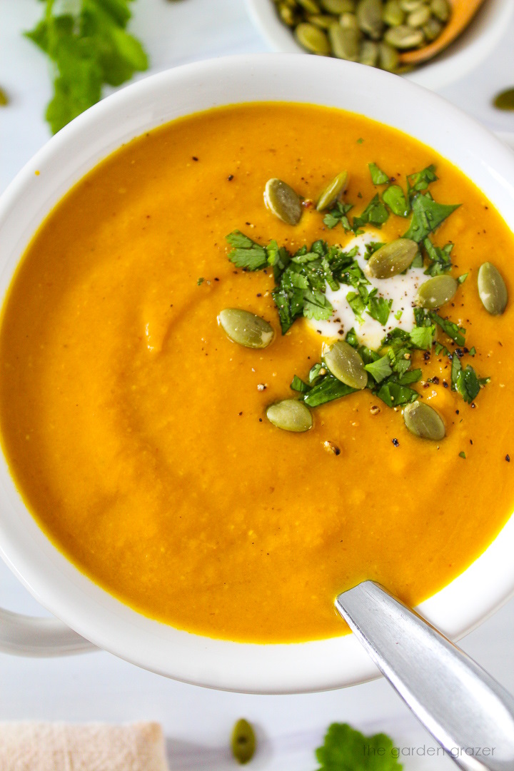 Close up view of pumpkin curry soup in a white serving bowl with fresh cilantro
