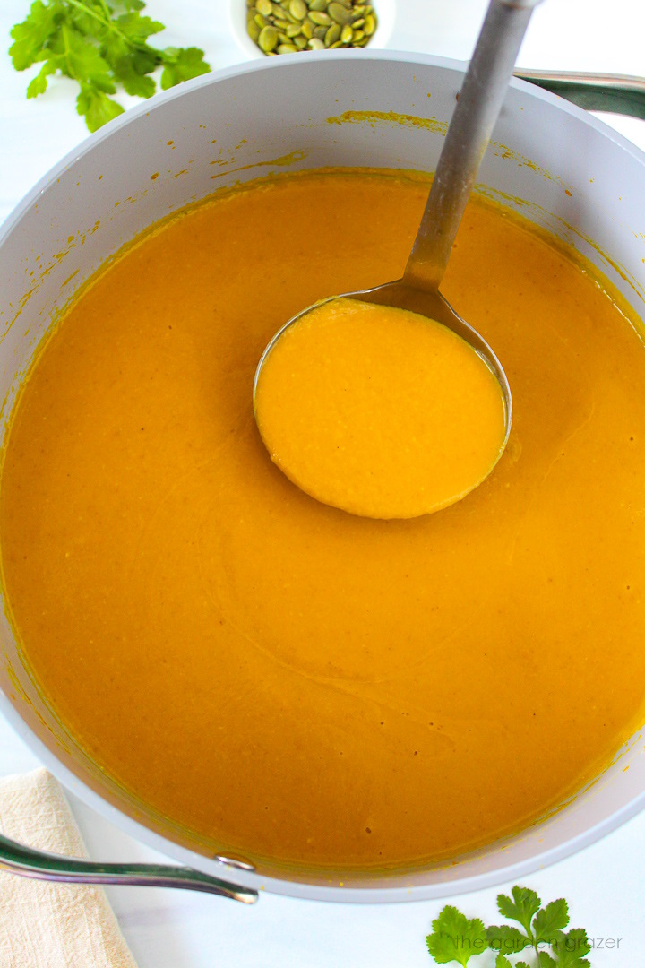 Overhead view of blended pumpkin curry soup cooking in a pot with a ladle