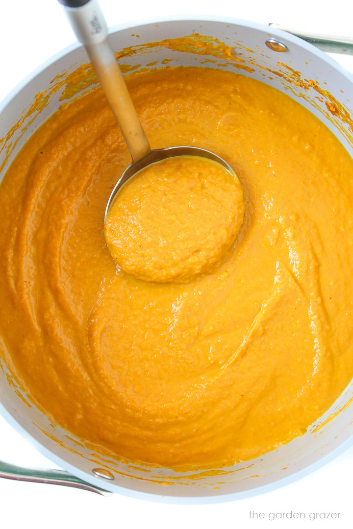 A ladle lifting up blended pumpkin curry soup from a large pot