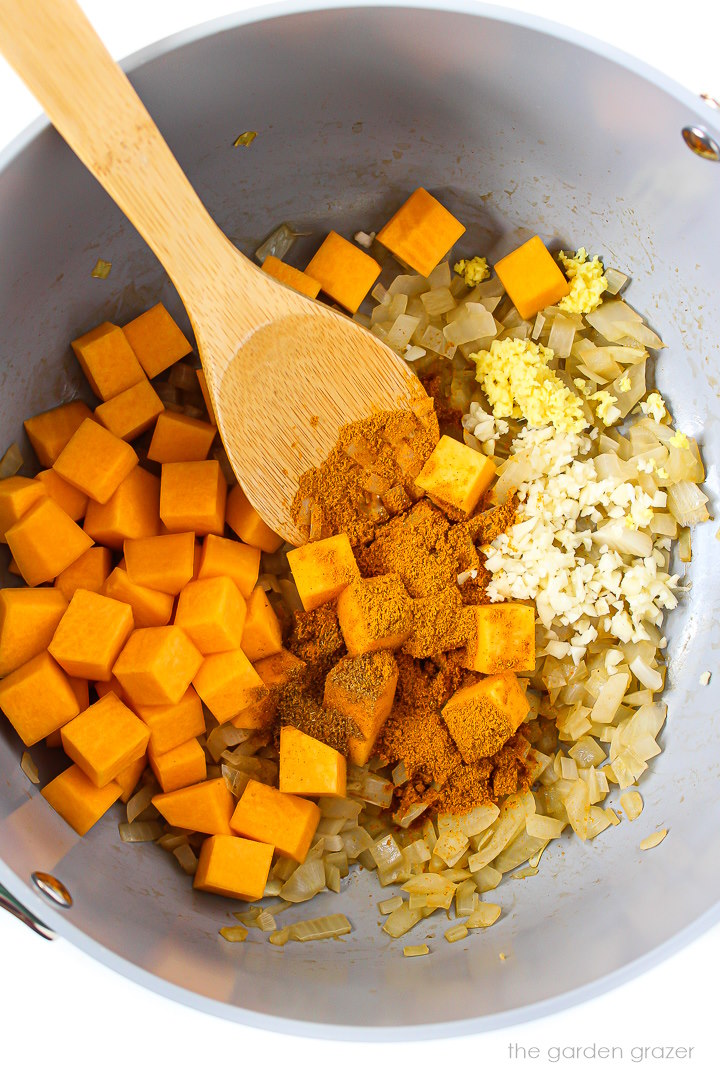 Overhead view of onion, garlic, ginger, butternut squash, and spices cooking in a pot