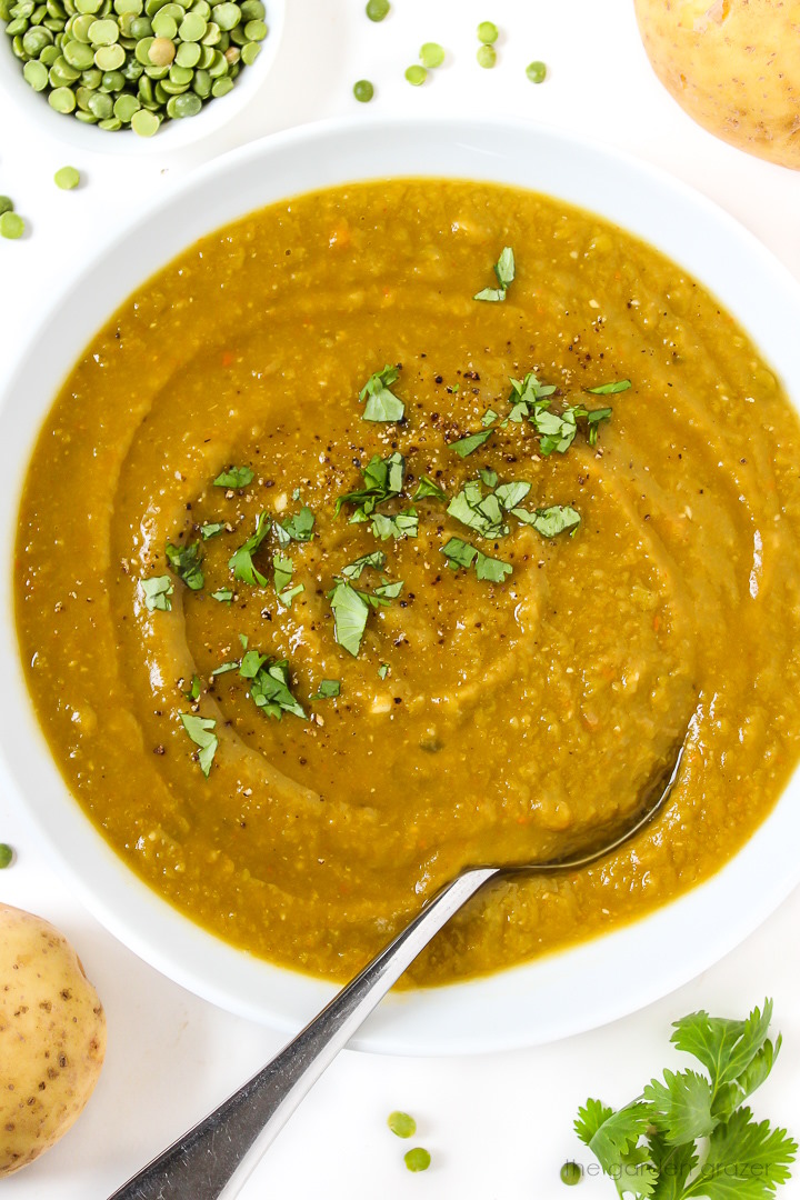 White bowl of vegan split pea potato soup garnished with fresh herbs and black pepper