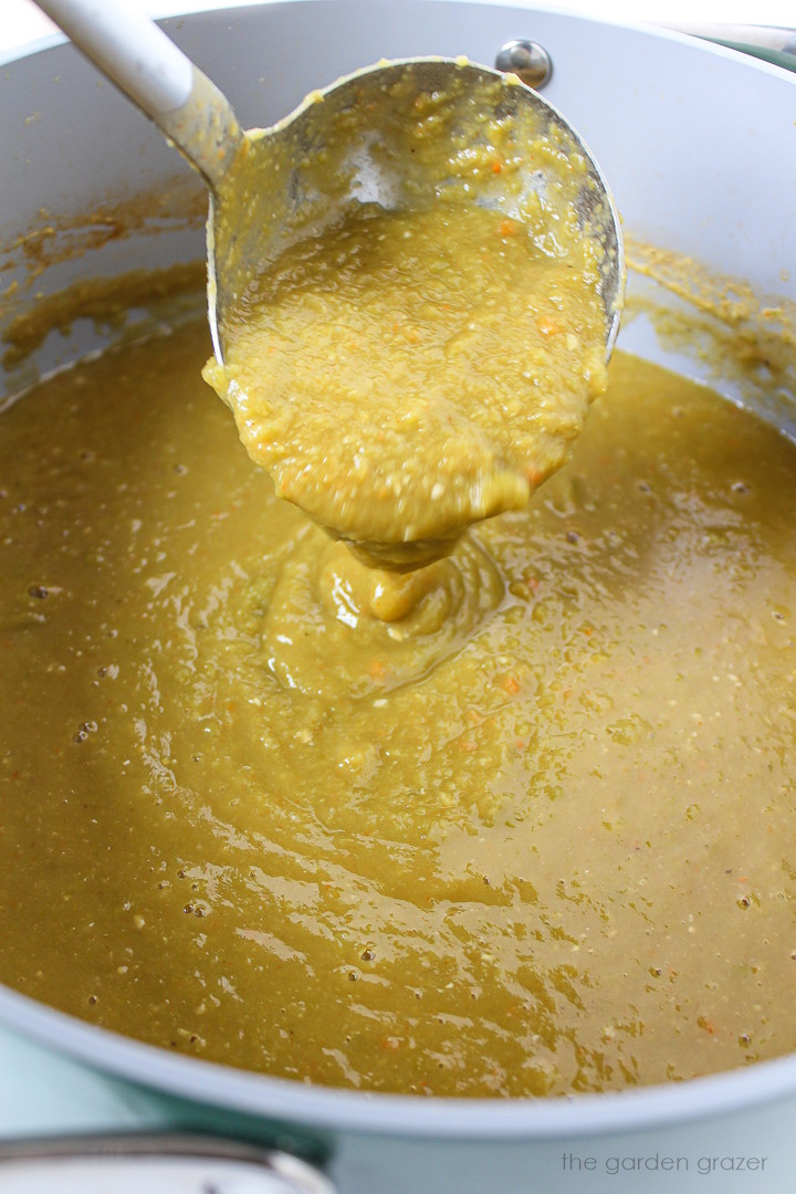 Ladle lifting up vegan split pea soup from a large pot during cooking
