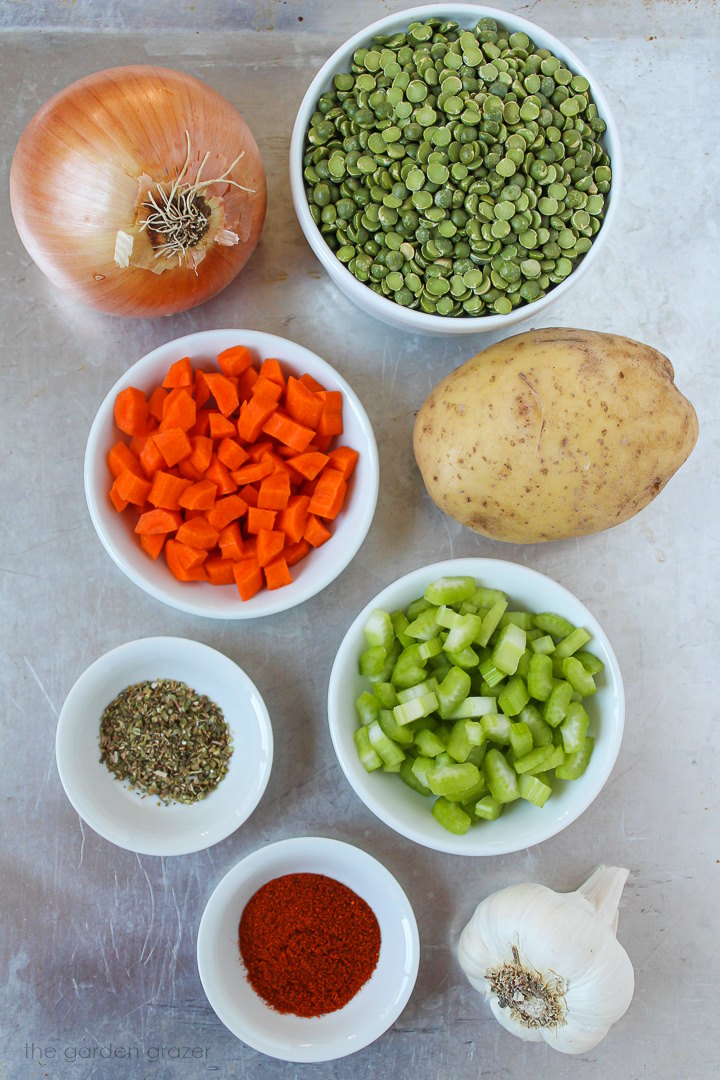 Dried peas, onion, potato, carrot, celery, and spice ingredients laid out on a metal tray