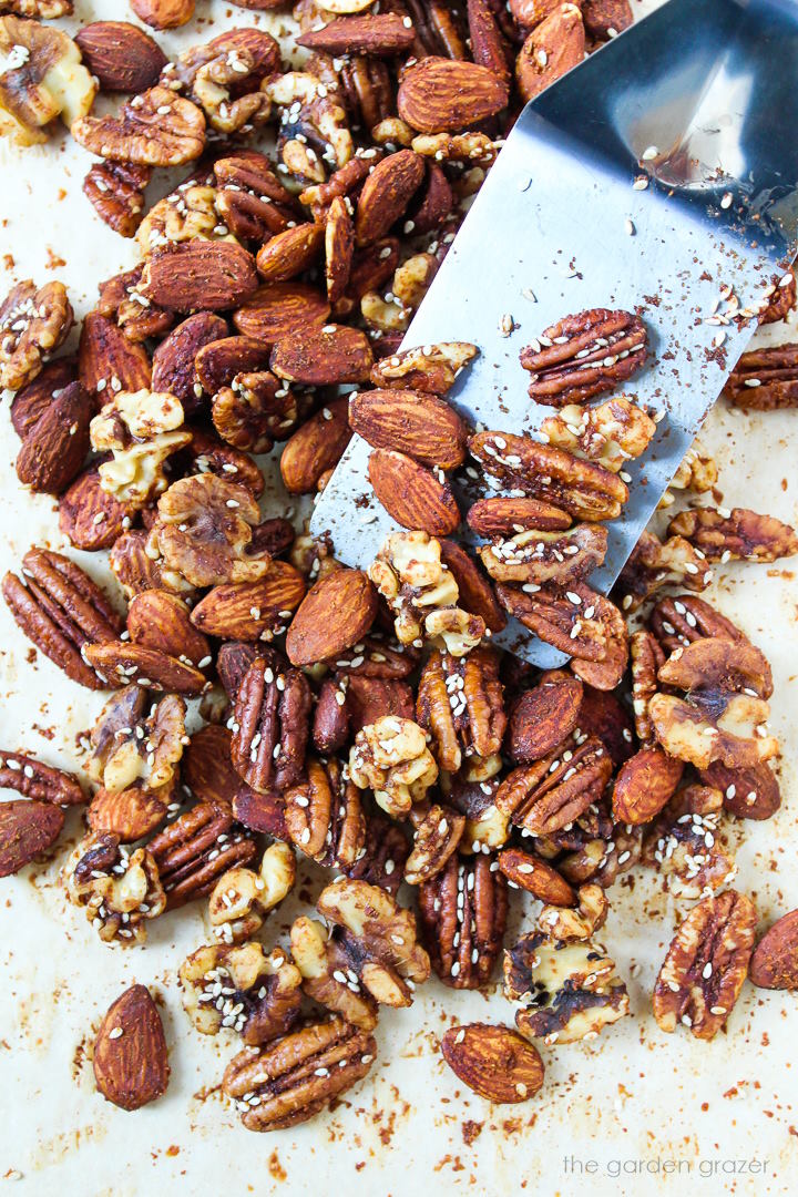 Savory tamari nuts roasting on a baking sheet with metal spatula for stirring