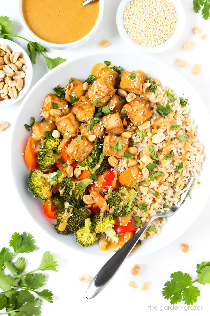 Overhead view of tofu rice bowl with roasted vegetables and topped with peanut sauce