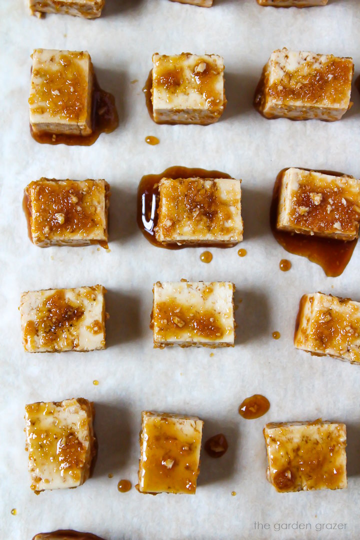 Savory marinated tofu cubes lined up on a sheet pan before baking