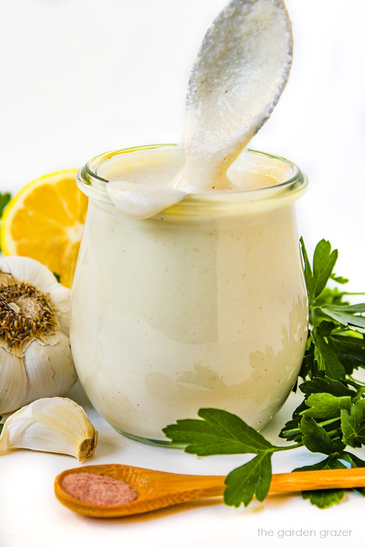 Vegan garlic aioli in a small glass jar with metal serving spoon