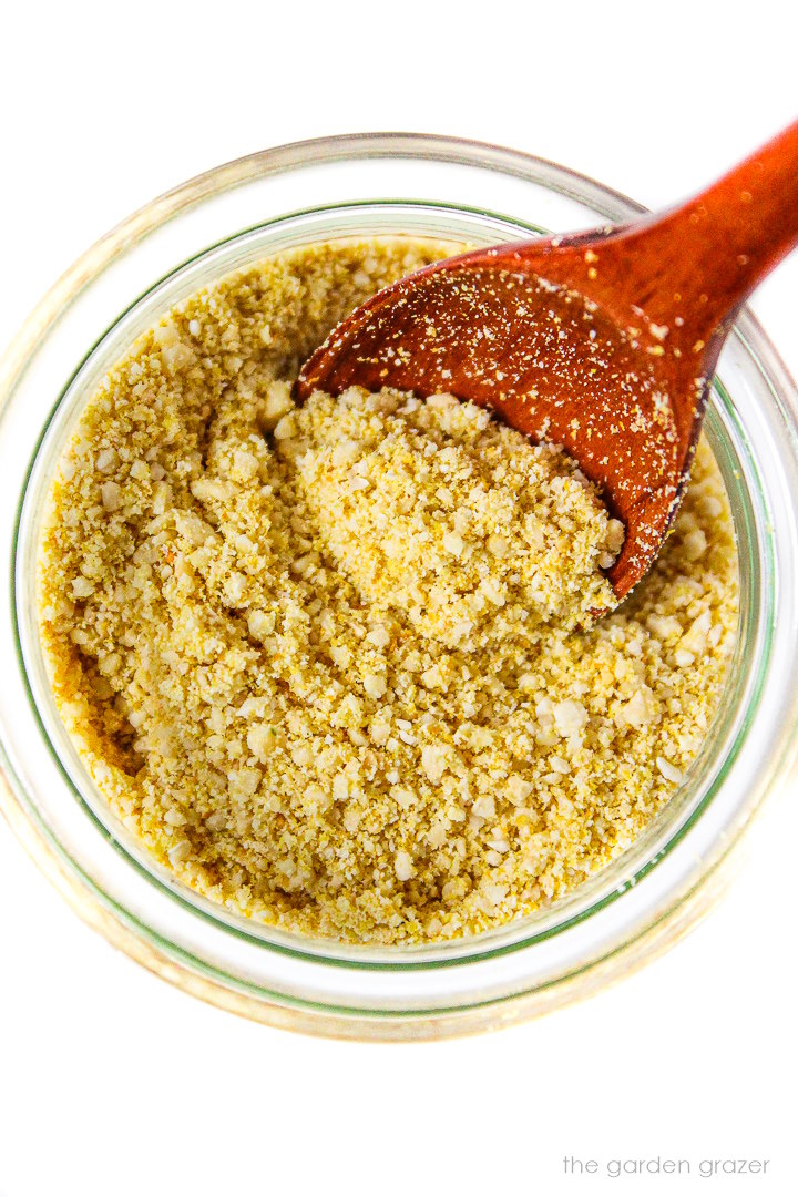 Close-up view of vegan parmesan cheese in a small glass jar with wooden spoon