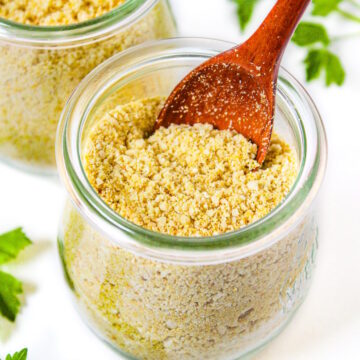 Two small glass jars of vegan parmesan cheese with wooden serving spoons