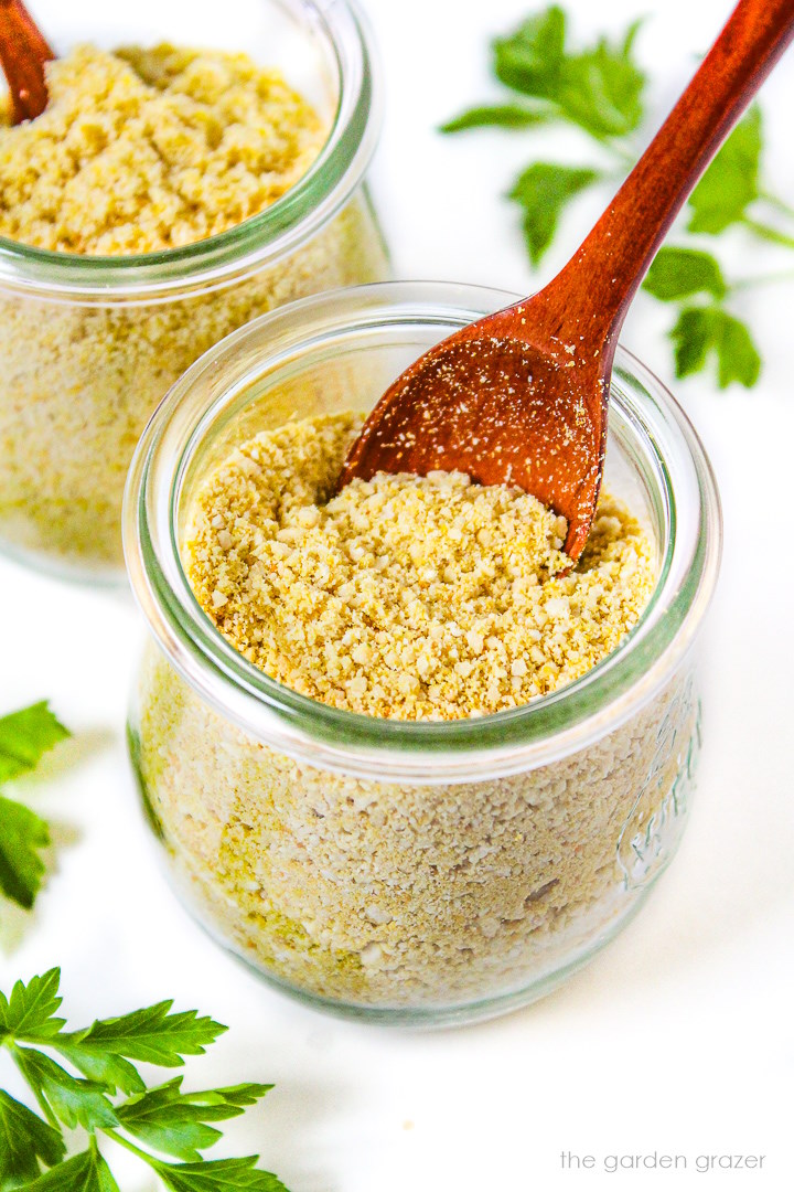 Two small glass jars of vegan parmesan cheese with wooden serving spoons