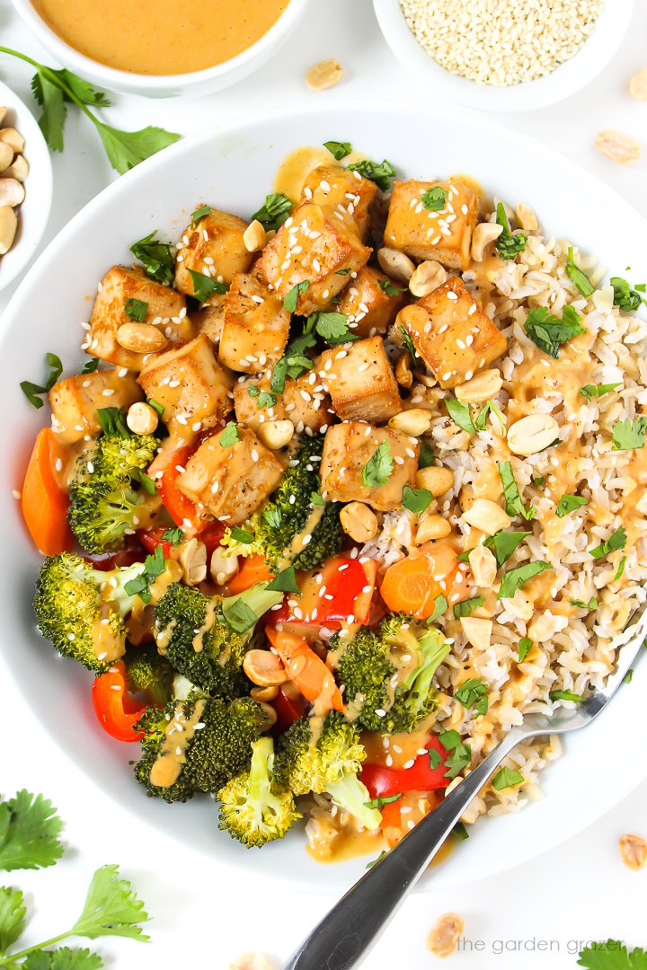 Close-up view of vegan rice and tofu bowl topped with peanut sauce, fresh cilantro, and sesame seeds.