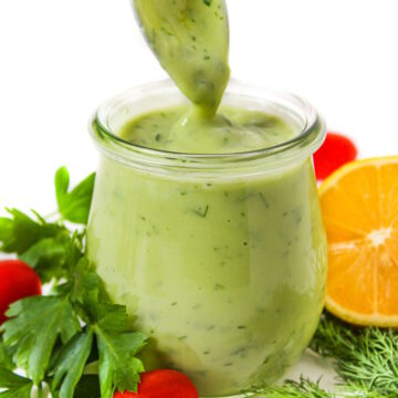 Side view of vegan avocado ranch dressing in a small glass jar with fresh herbs