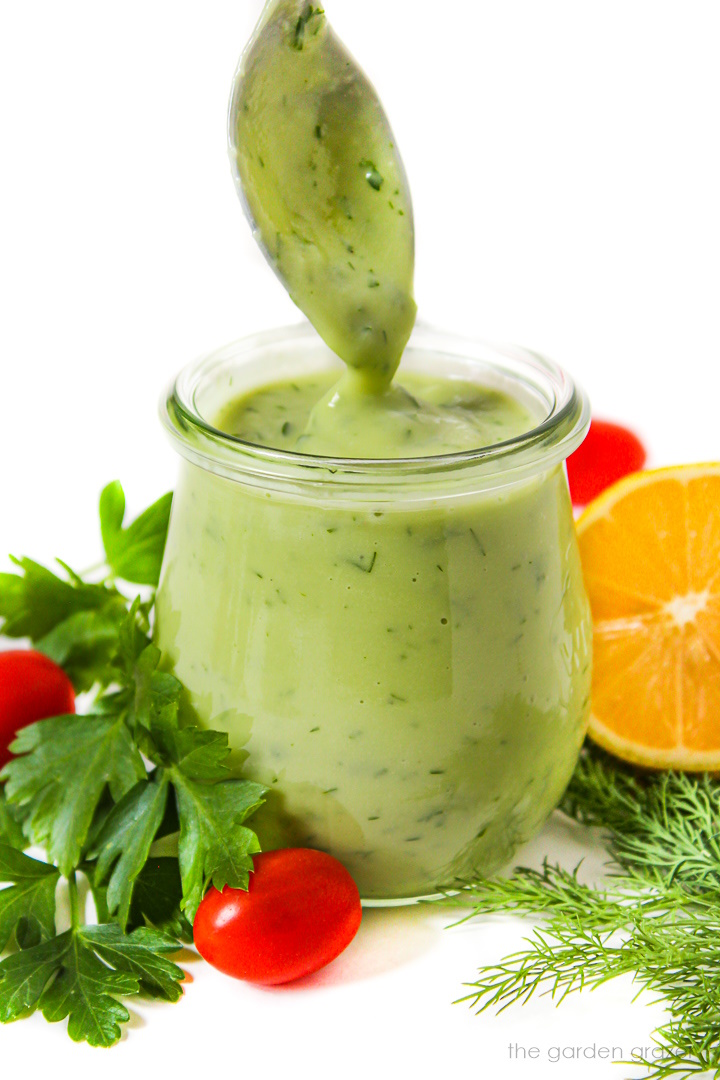 Side view of vegan avocado ranch dressing in a small glass jar with fresh herbs
