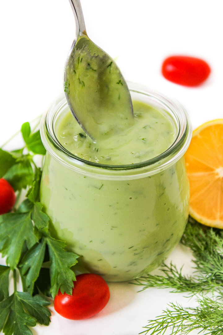 Spoon lifting up vegan avocado ranch dressing from a small glass jar