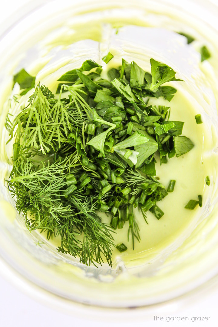 Overhead view of fresh herbs in a blender cup before being blended into dressing