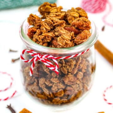 Vegan gingerbread granola in a small glass jar with cinnamon sticks and cloves on the side