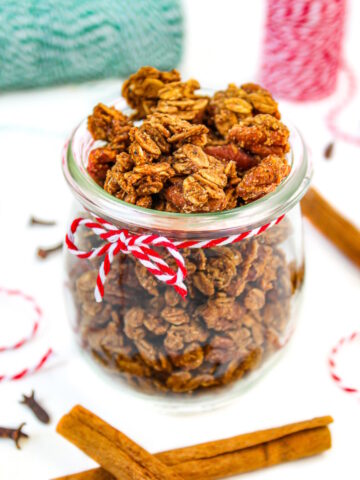 Vegan gingerbread granola in a small glass jar with cinnamon sticks and cloves on the side