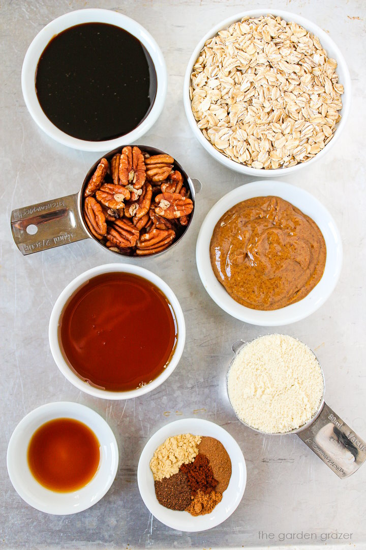 Oats, pecans, almond butter, molasses, maple syrup, and spice ingredients laid out on a metal tray