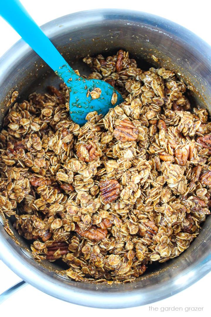 Overhead view of gingerbread granola mixed together in a saucepan before baking