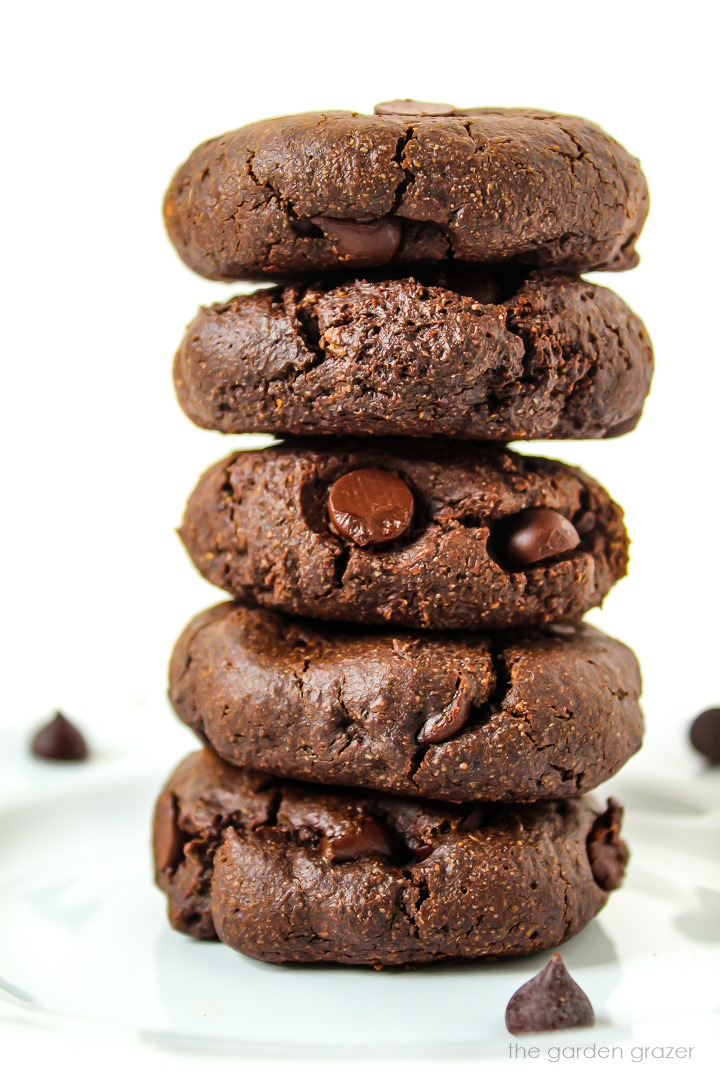 Five vegan double chocolate cookies stacked on a white plate