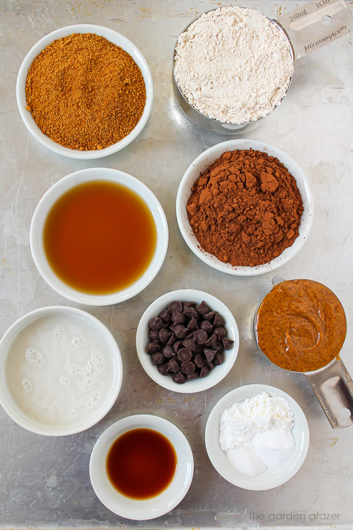 Oat flour, almond butter, coconut sugar, maple syrup, milk, vanilla extract, and baking powder ingredients laid out on a metal tray