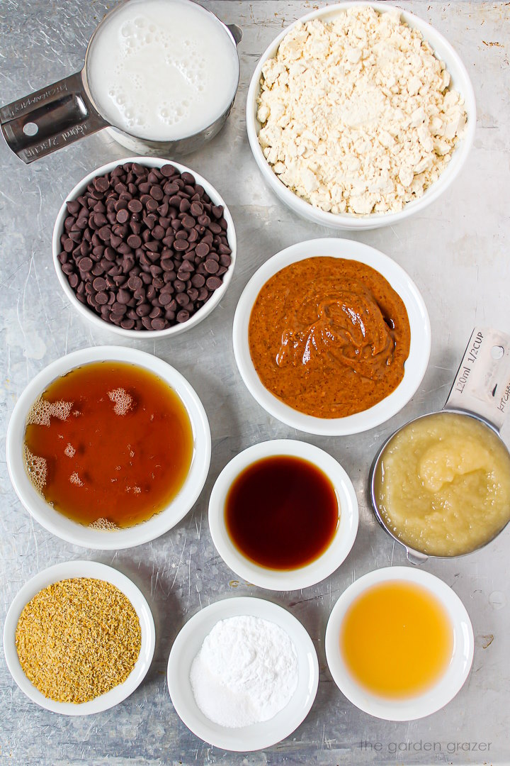 Gluten-free flour, chocolate, dairy-free milk, almond butter, maple syrup, applesauce, and vanilla ingredients laid out on a metal tray