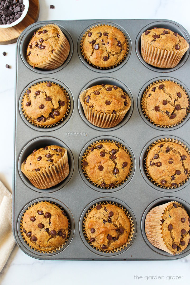 A dozen baked vegan chocolate chip muffins resting in a muffin pan