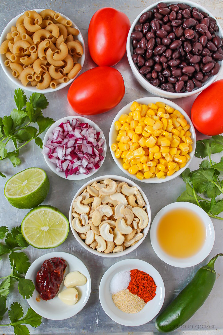 Elbow noodles, black beans, tomatoes, corn, onion, cashews, and spice ingredients laid out on a metal tray