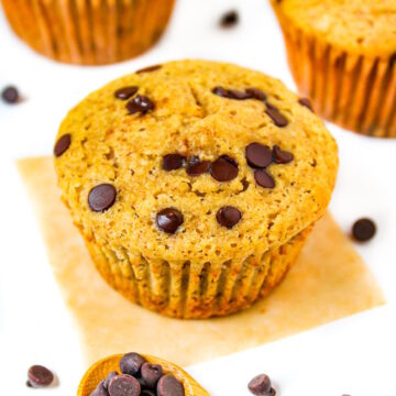 Three vegan chocolate chip muffins on a white table with chocolate chips scattered