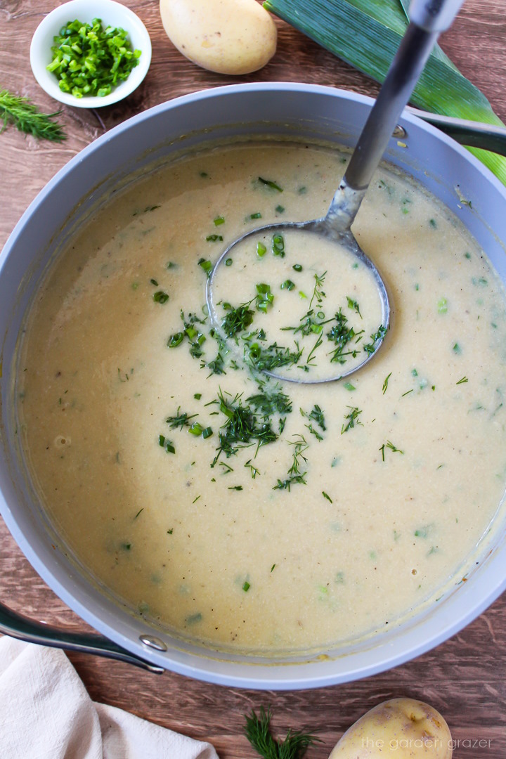 Overhead view of a ladle lifting up blended vegan potato leek soup from a large pot after it cooks