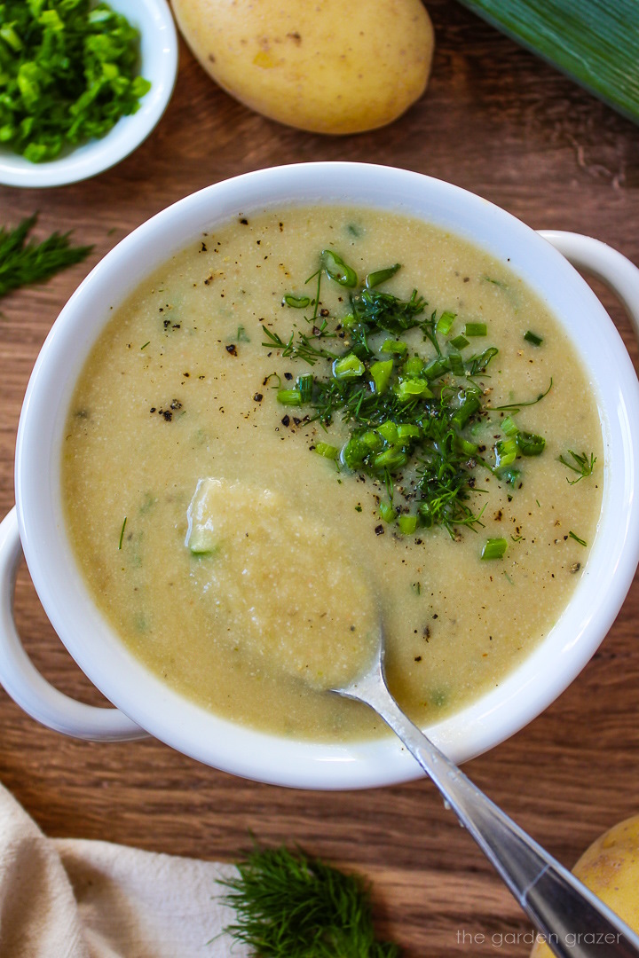 A serving spoon lifting up vegan potato leek soup from a white bowl