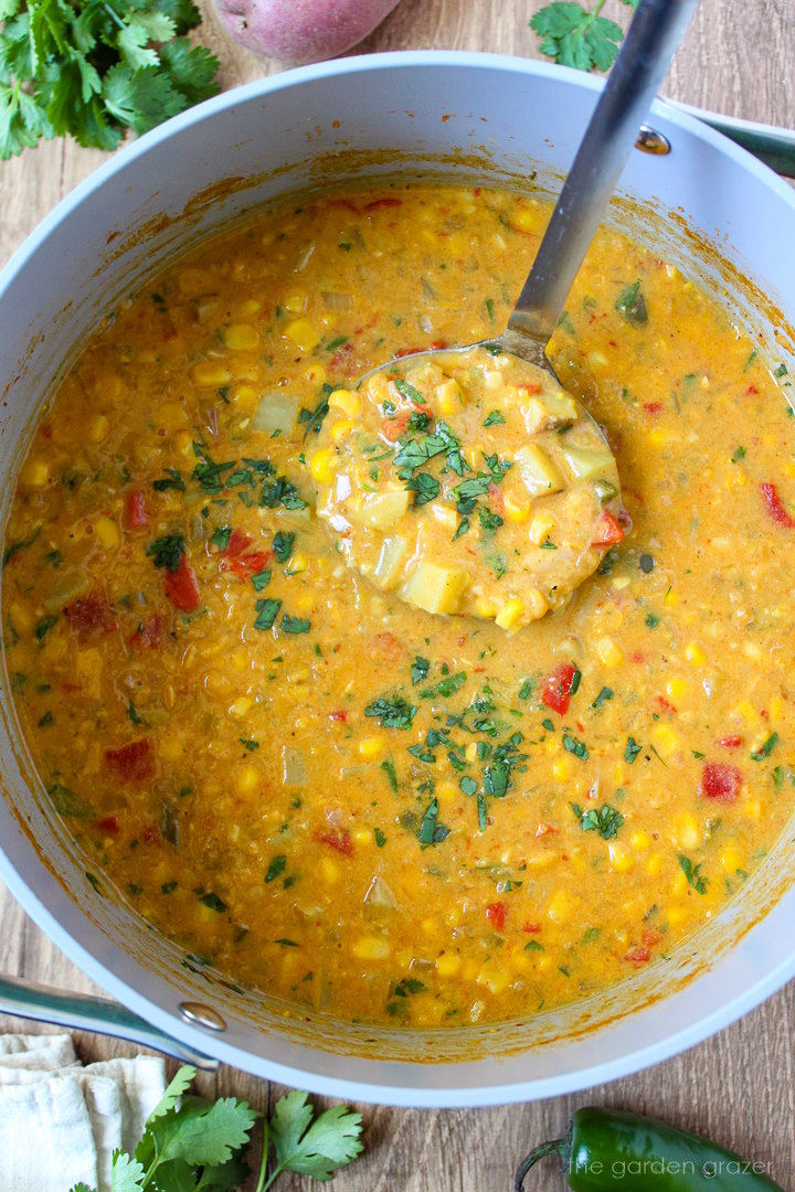 Soup ladle lifting up southwest corn chowder from a large pot as it cooks