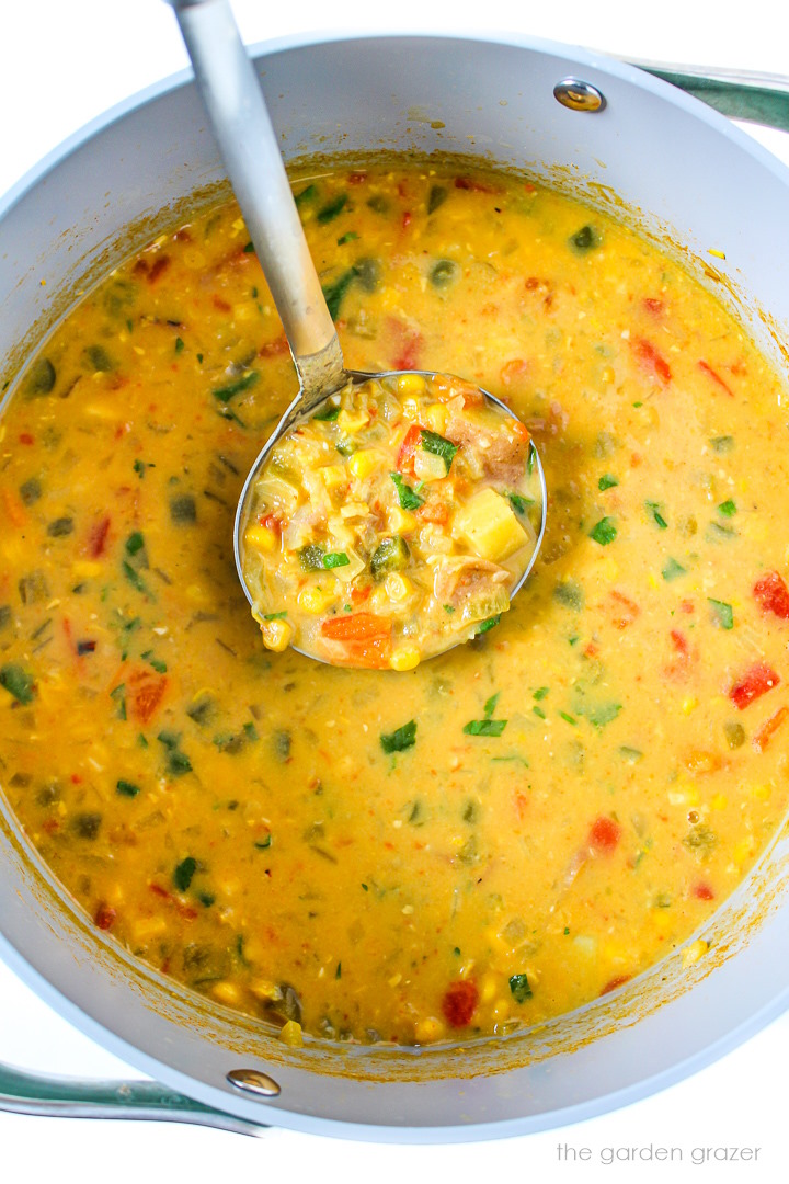 Overhead view of a ladle lifting up vegan southwest corn chowder as it cooks in a large pot