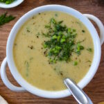Vegan potato leek soup in a white serving bowl garnished with chives and fresh dill