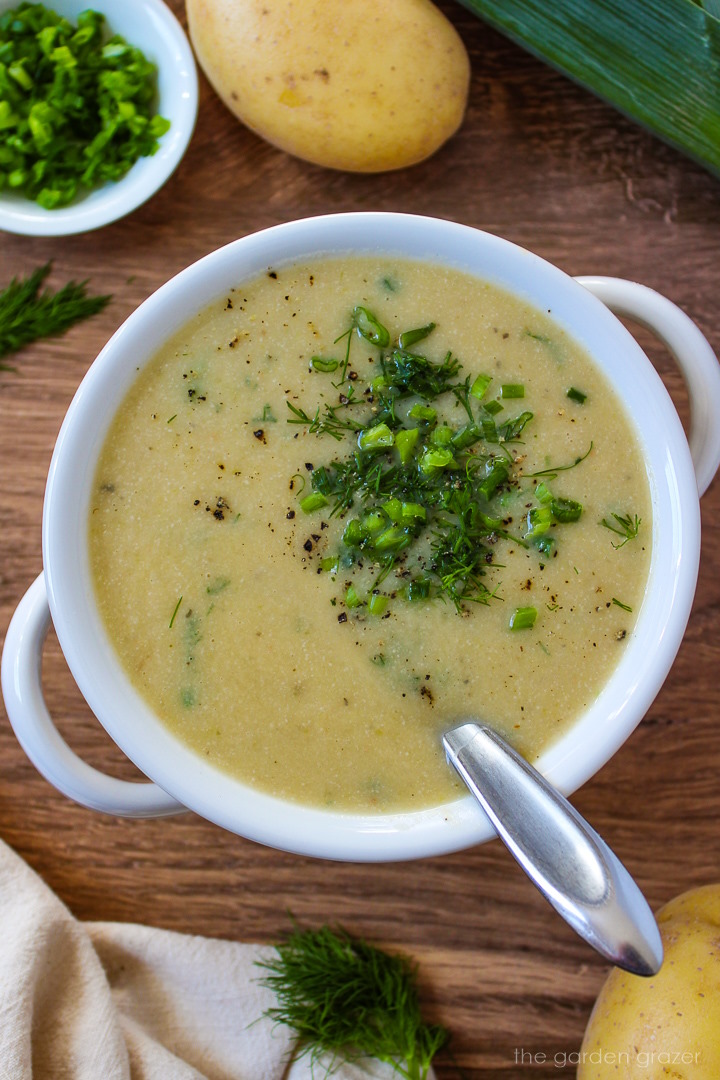 Vegan potato leek soup in a white serving bowl garnished with chives and fresh dill