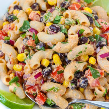 Close-up view of vegan southwest pasta salad on a white plate with serving spoon