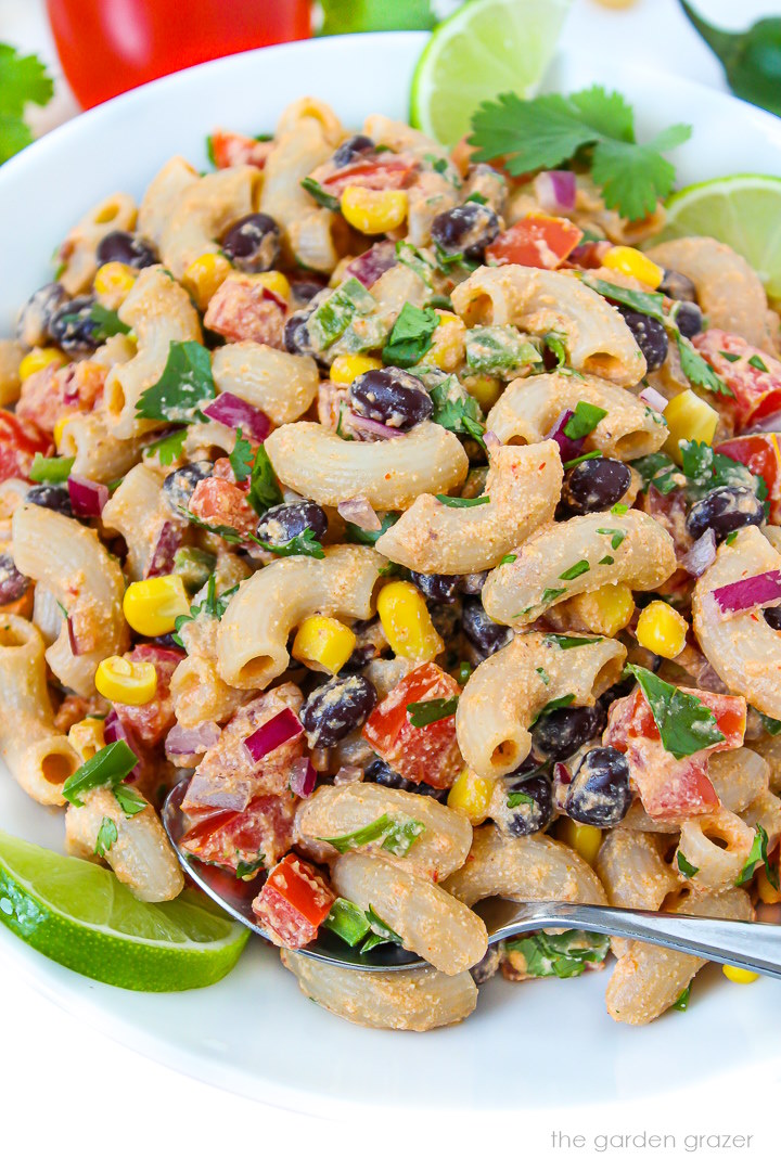 Close-up view of vegan southwest pasta salad on a white plate with serving spoon