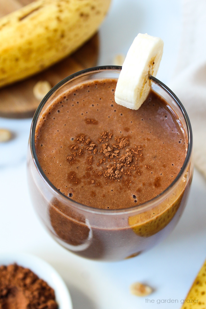 Vegan chunky monkey protein smoothie in a serving glass topped with cocoa powder and banana slice